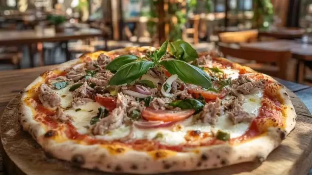 Pizza au thon avec mozzarella, tomates fraîches, basilic, et thon émietté, dans un restaurant italien ensoleillé avec une ambiance chaleureuse.
