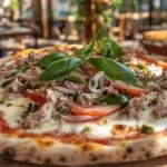 Pizza au thon avec mozzarella, tomates fraîches, basilic, et thon émietté, dans un restaurant italien ensoleillé avec une ambiance chaleureuse.