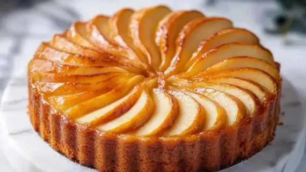 Gâteau aux pommes doré avec des tranches fines disposées en spirale, sur un plat en marbre.