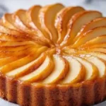 Gâteau aux pommes doré avec des tranches fines disposées en spirale, sur un plat en marbre.