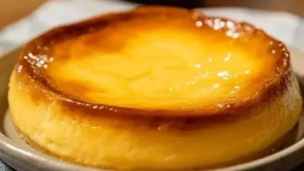 Œufs au lait cuits au four, surface lisse et brillante, bords caramélisés, grand flan doré posé sur une assiette grise, lumière chaude.