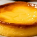 Œufs au lait cuits au four, surface lisse et brillante, bords caramélisés, grand flan doré posé sur une assiette grise, lumière chaude.