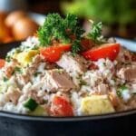 Salade de riz avec morceaux de thon, légumes frais comme des tomates et des concombres, garnie de persil frais.