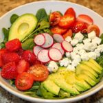 Salade d'amour avec avocat, radis, tomates cerises, fraises et fromage feta sur un lit de jeunes pousses d'épinards, assaisonnée de poivre noir fraîchement moulu.