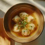 Bol de soupe won ton avec raviolis chinois farcis de crevettes, bouillon clair, graines de sésame et ciboulette fraîche, vue de dessus.