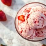 Boules de glace maison à la fraise dans une coupe en verre, entourées de fraises fraîches, vue de dessus, éclairage naturel.