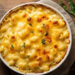 Gratin de macaronis au fromage doré avec des herbes fraîches, présenté dans un plat blanc sur une table en bois.