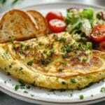 Omelette soufflée dorée garnie de persil frais, servie avec salade verte et tomates cerises, accompagnée de tranches de pain grillé.