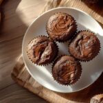 Muffins moelleux au Nutella avec un cœur fondant, présentés dans une assiette blanche sur une planche en bois, lumière naturelle.
