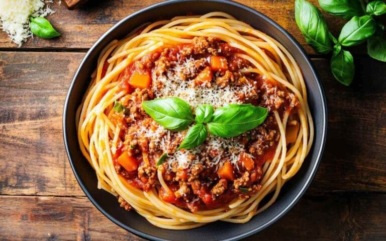Assiette de spaghetti nappés d’une sauce bolognaise maison garnie de morceaux de carottes, de viande hachée, de parmesan râpé et décorée de feuilles de basilic frais, sur une table en bois rustique.