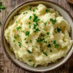 Purée de pommes de terre maison onctueuse dans un bol en céramique, garnie de persil frais haché, posée sur une table en bois rustique.