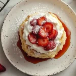 Shortcake aux fraises vu du dessus : biscuit doré nappé de sirop, chantilly vanillée, fraises tranchées et sucre glace, sur assiette mouchetée.