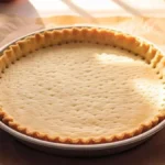 Pâte brisée maison cuite à blanc dans un moule à tarte, dorée et prête à garnir pour une tarte sucrée ou salée.