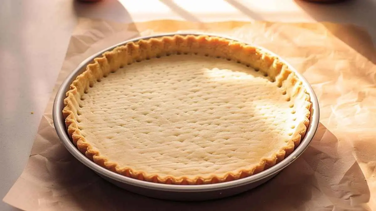 Pâte brisée maison cuite à blanc dans un moule à tarte, dorée et prête à garnir pour une tarte sucrée ou salée.