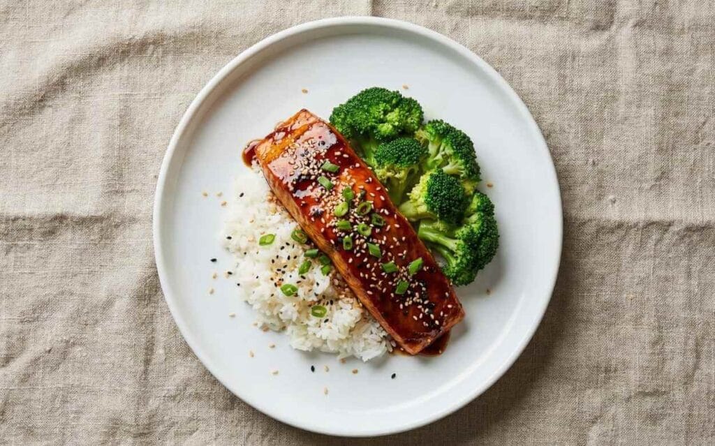 Plat de saumon glacé à la sauce soja/miel, riz blanc et brocolis à la vapeur, garni de graines de sésame et de ciboulette, vue de dessus.