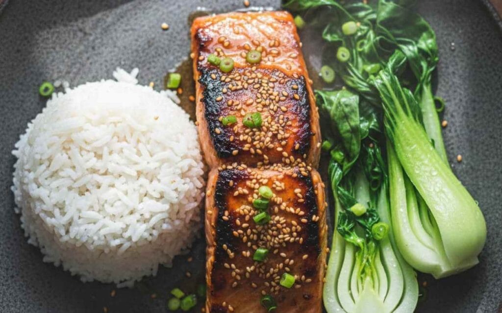 Deux filets de saumon glacé au miel et graines de sésame, servis avec du riz blanc et du bok choy.