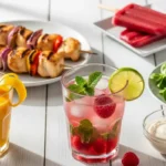 Repas d'été avec des brochettes de poulet grillées, une salade, une boisson jaune, et un cocktail de fruits rouges.